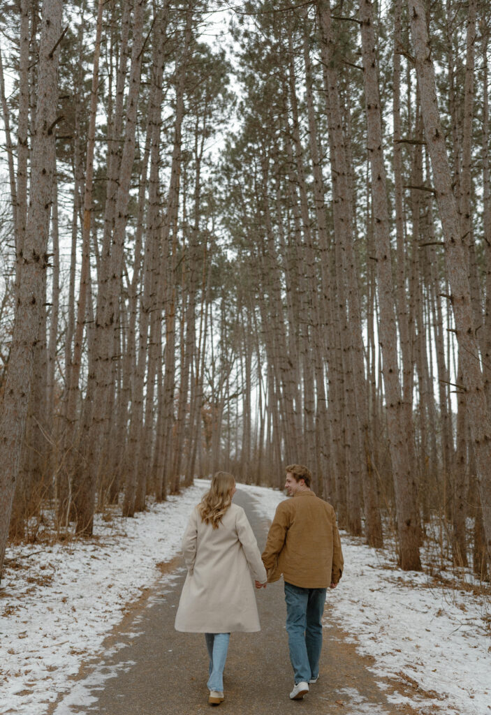 Couple walking hand in hand through pine trees at Rice Creek Regional Park in winter