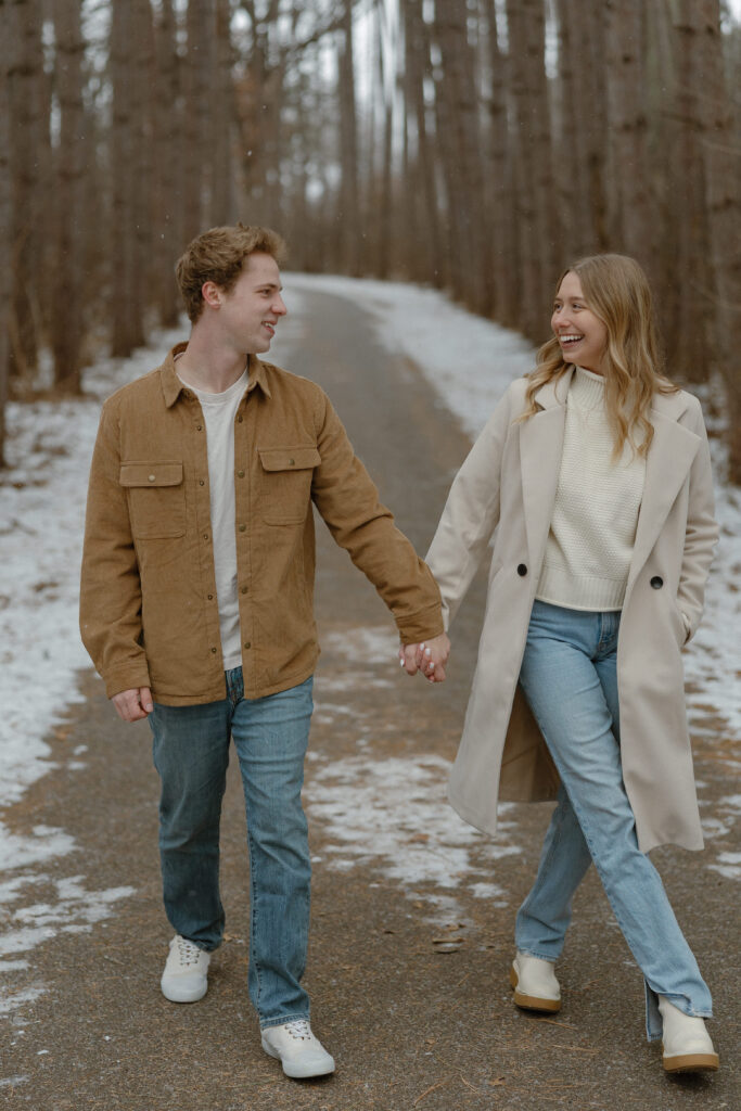 Couple walking hand in hand through pine trees at Rice Creek Regional Park in winter