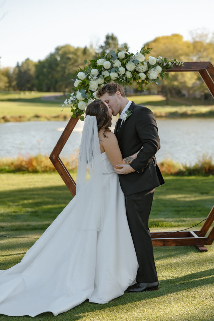 Bride and grooms first kiss at outdoor waterfront ceremony at Oak Glen Golf Course wedding Stillwater MN