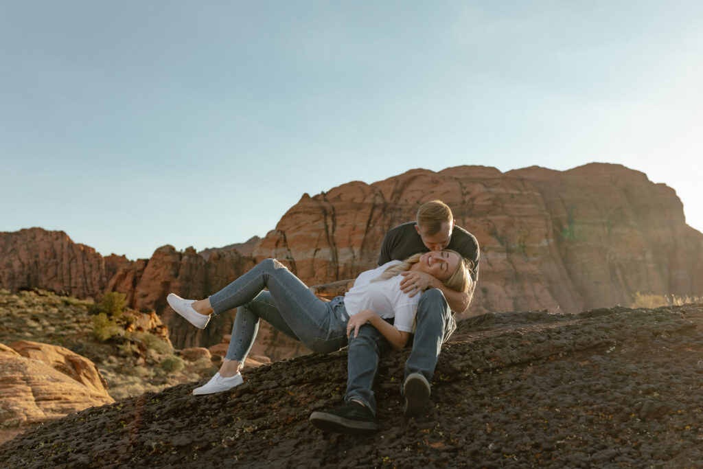 Bridget and Brandon sitting together on red rock cliffs during their Snow Canyon State Park day before session