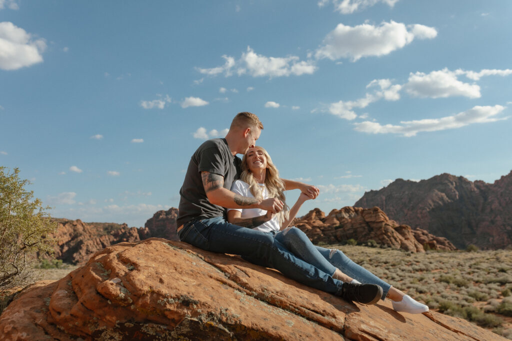 Bridget and Brandon sitting together on red rock cliffs during their Snow Canyon State Park day before session